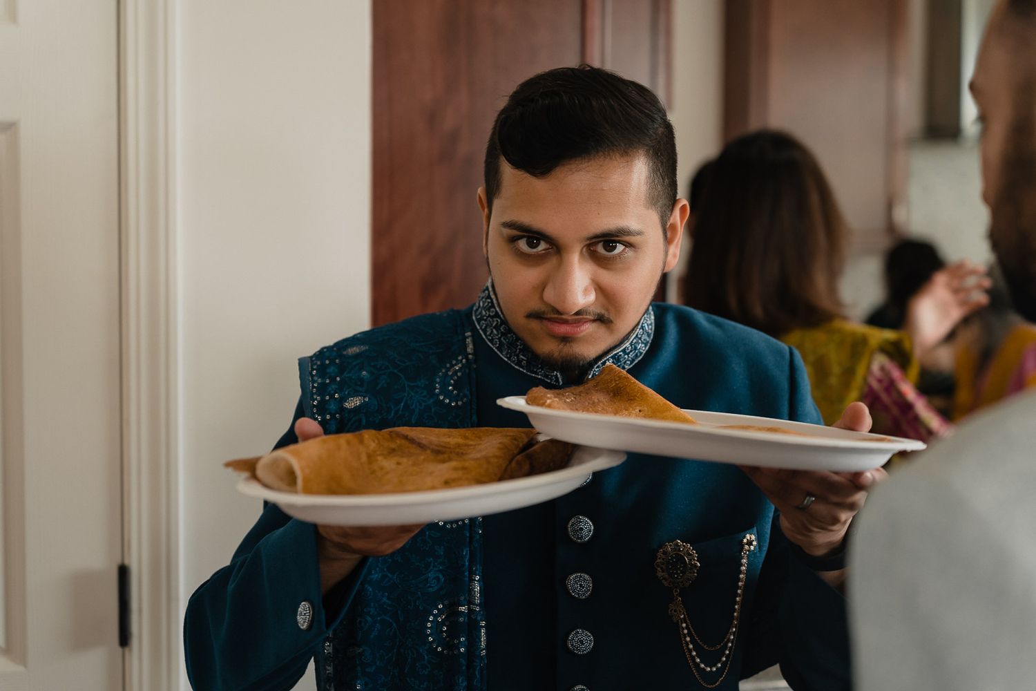 Server holds up wooden serving platter with food in denim jacket while working at restaurant.