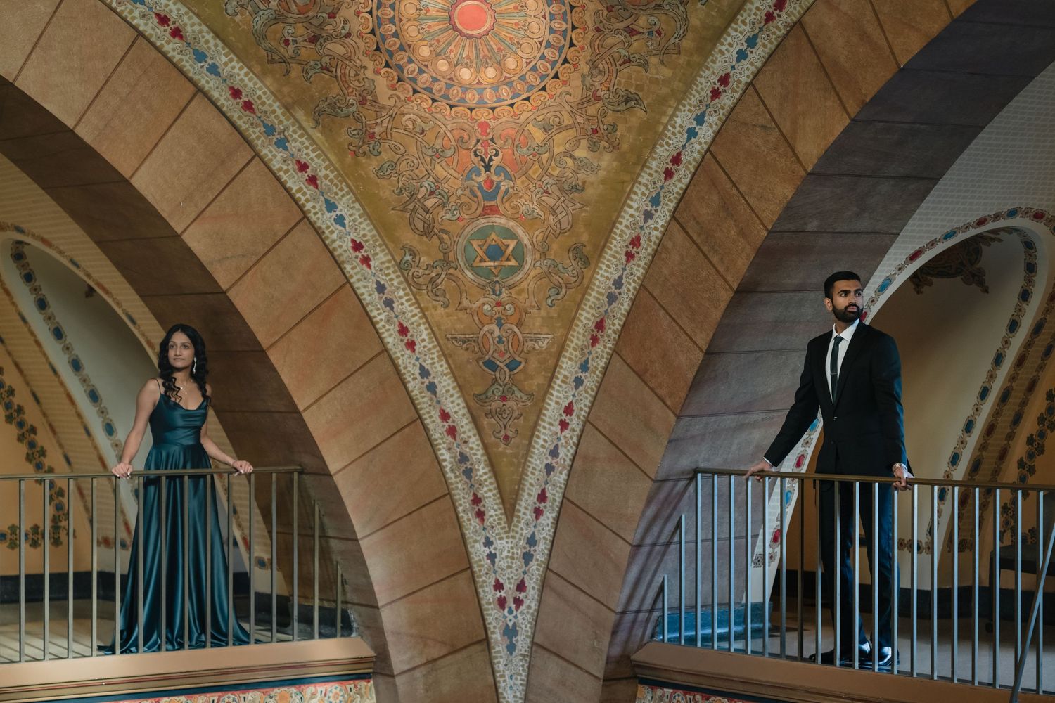 Couple posing separately in ornate arched hallway with decorative ceiling.