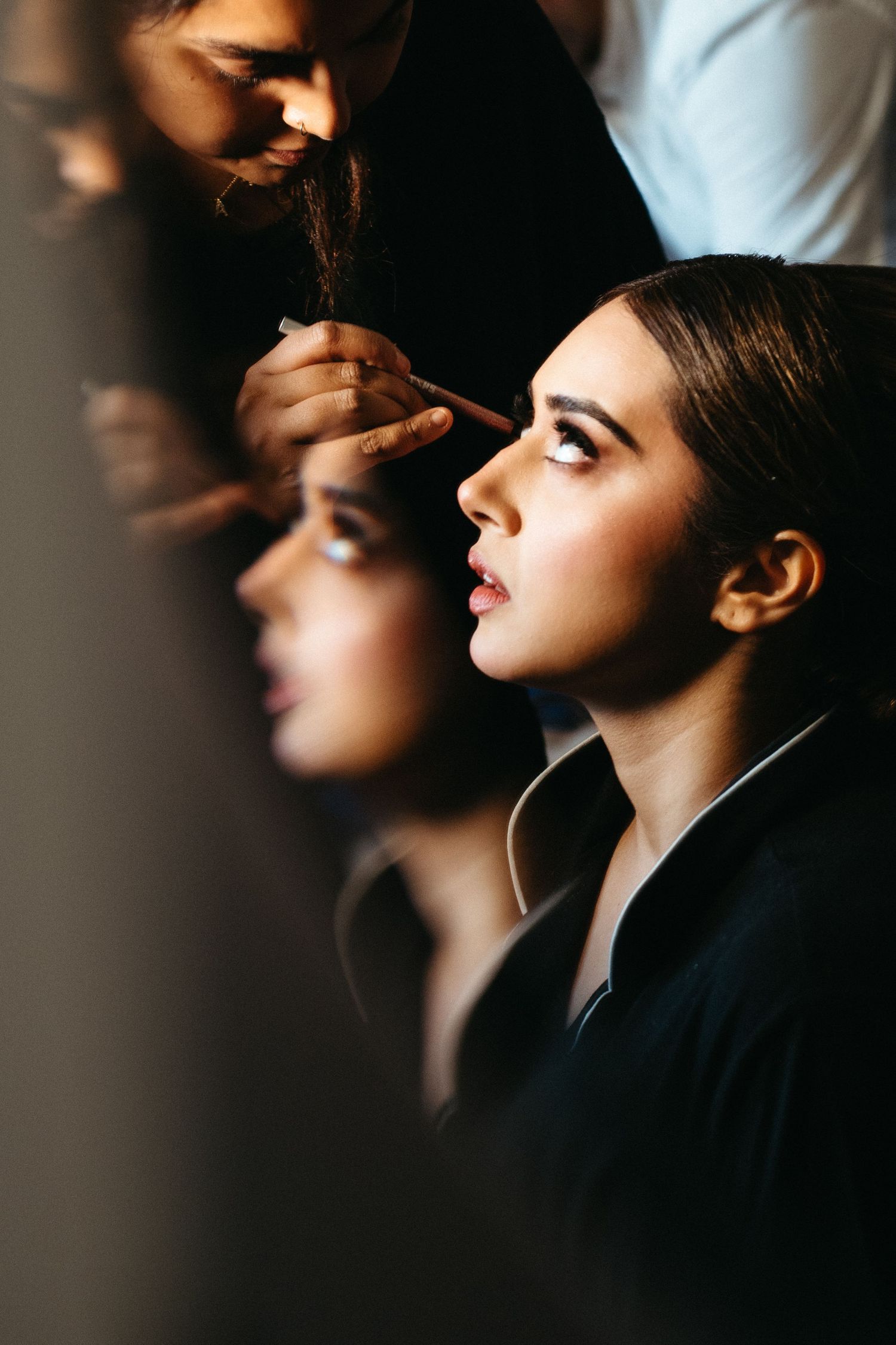 A profile shot of someone getting professional makeup applied in dramatic lighting.