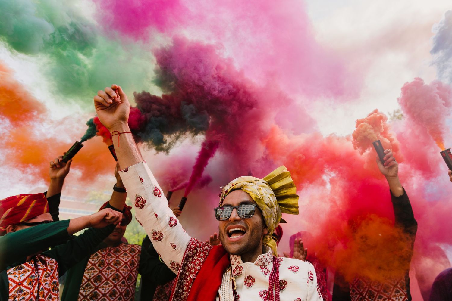 Colorful holi powder celebration at Indian wedding with vibrant pink and orange clouds.
