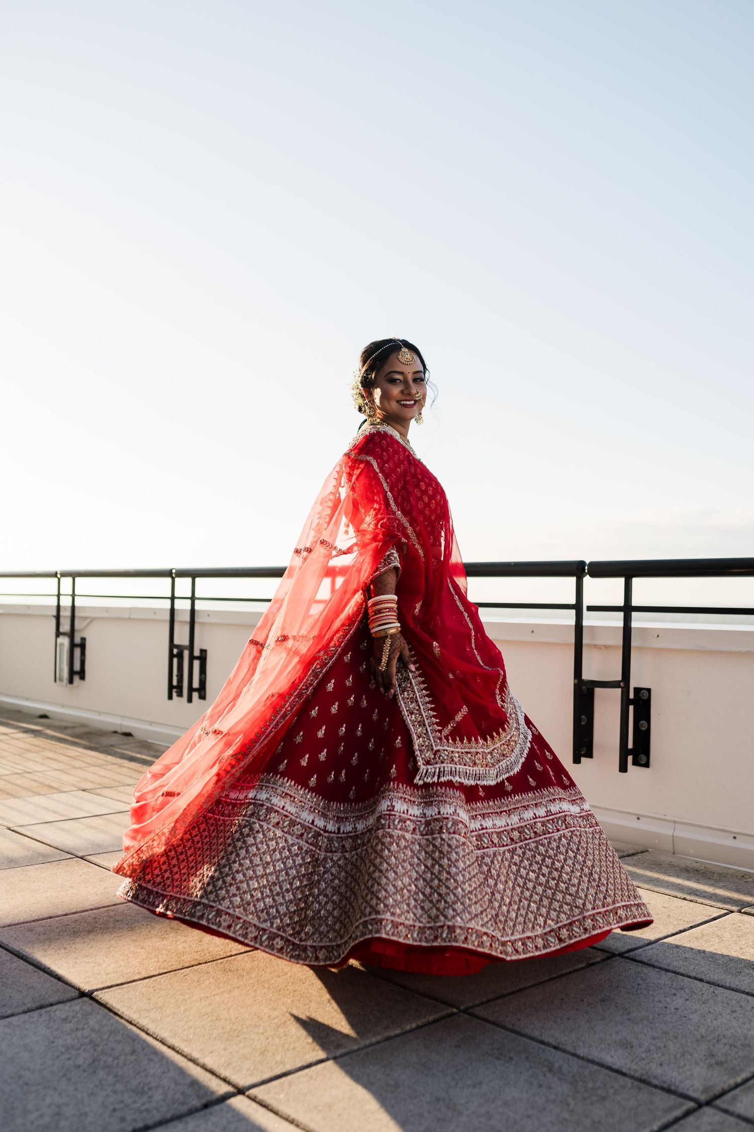 Traditional red and white lehenga twirls elegantly against modern rooftop backdrop.