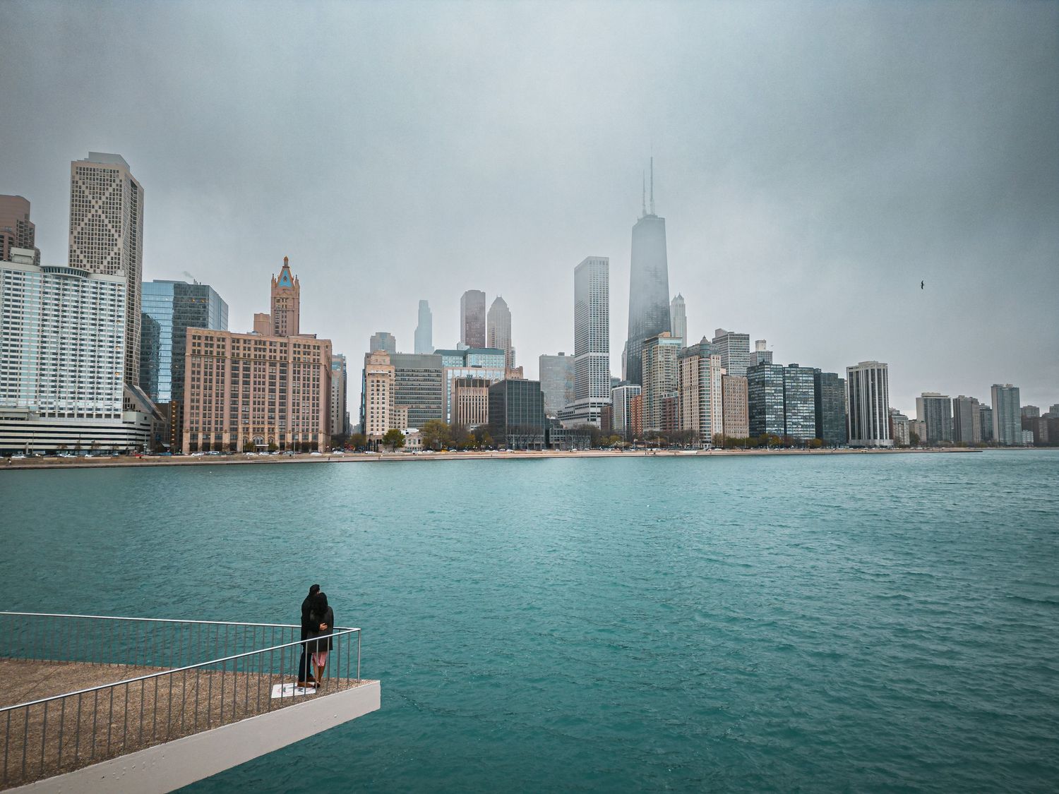 Chicago skyline view across turquoise waters with a lone figure standing on the pier.