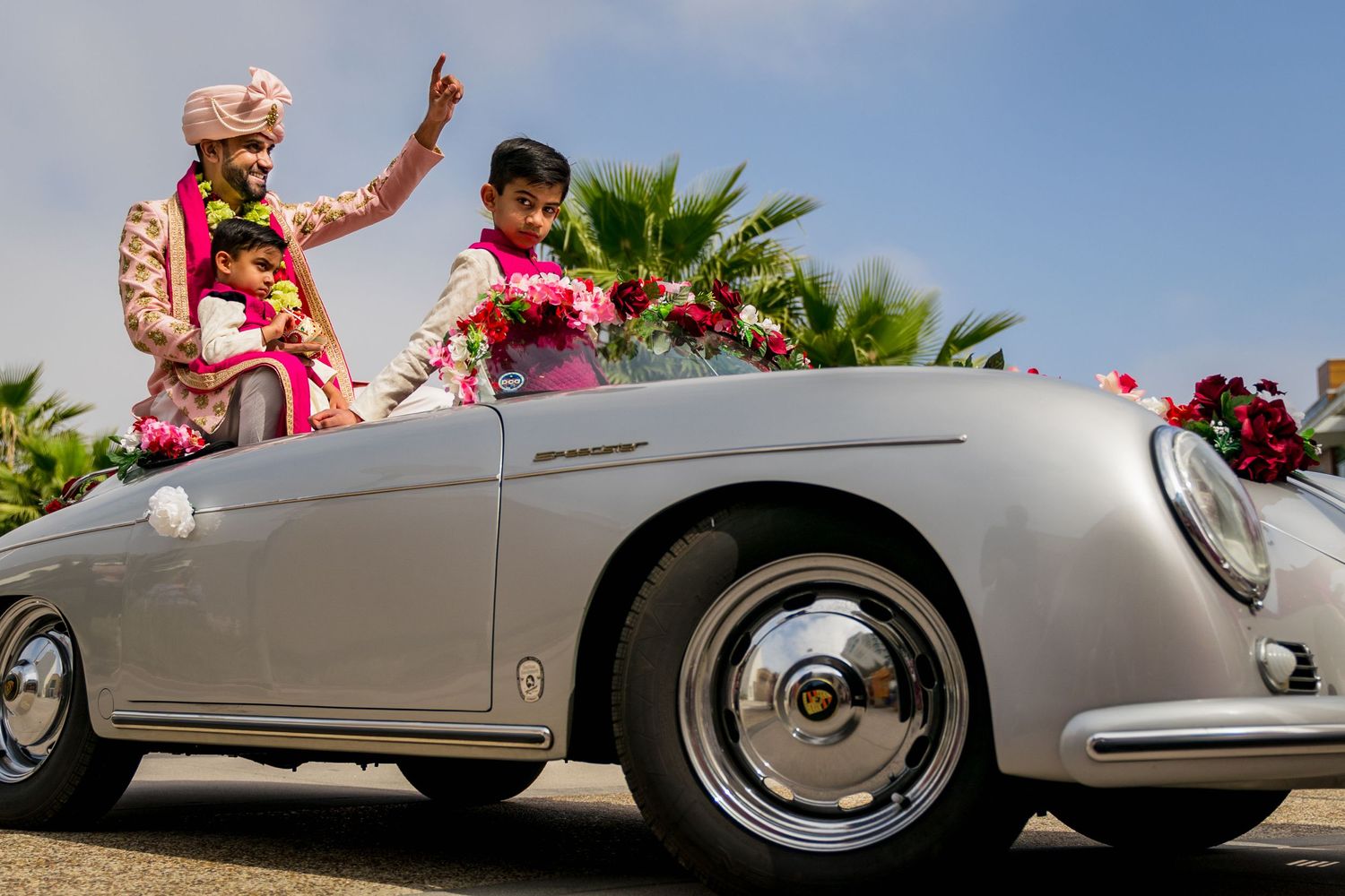 A classic silver Porsche 356 Speedster decorated with flowers carries celebrants during a wedding.