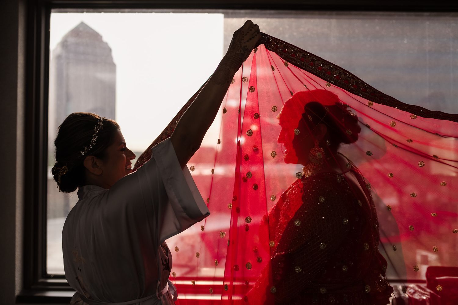 A silhouette of two people by a window with a flowing red veil creating a dramatic effect.