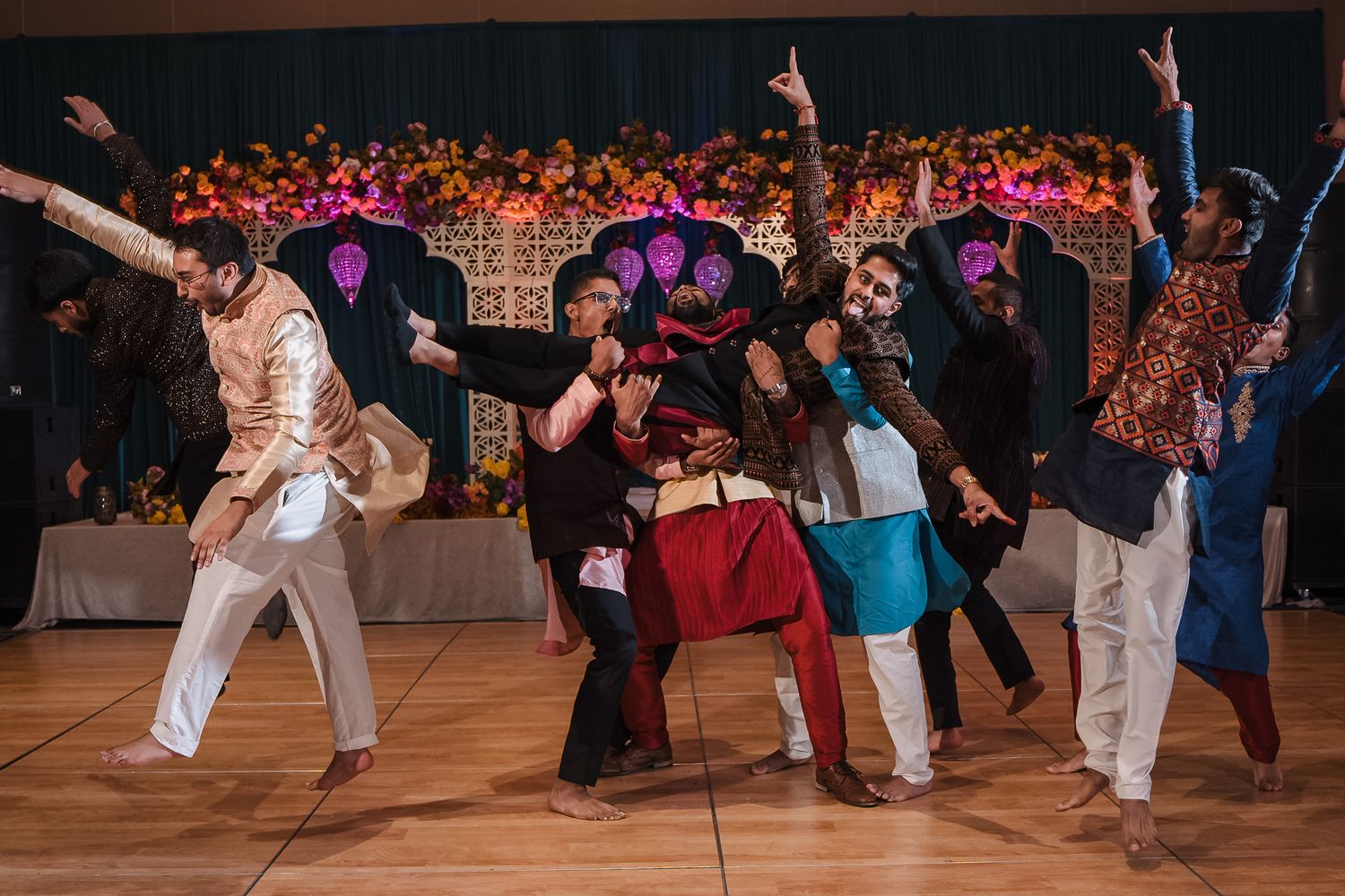 People dancing energetically at a party on a wooden dance floor with colorful lights in the background.