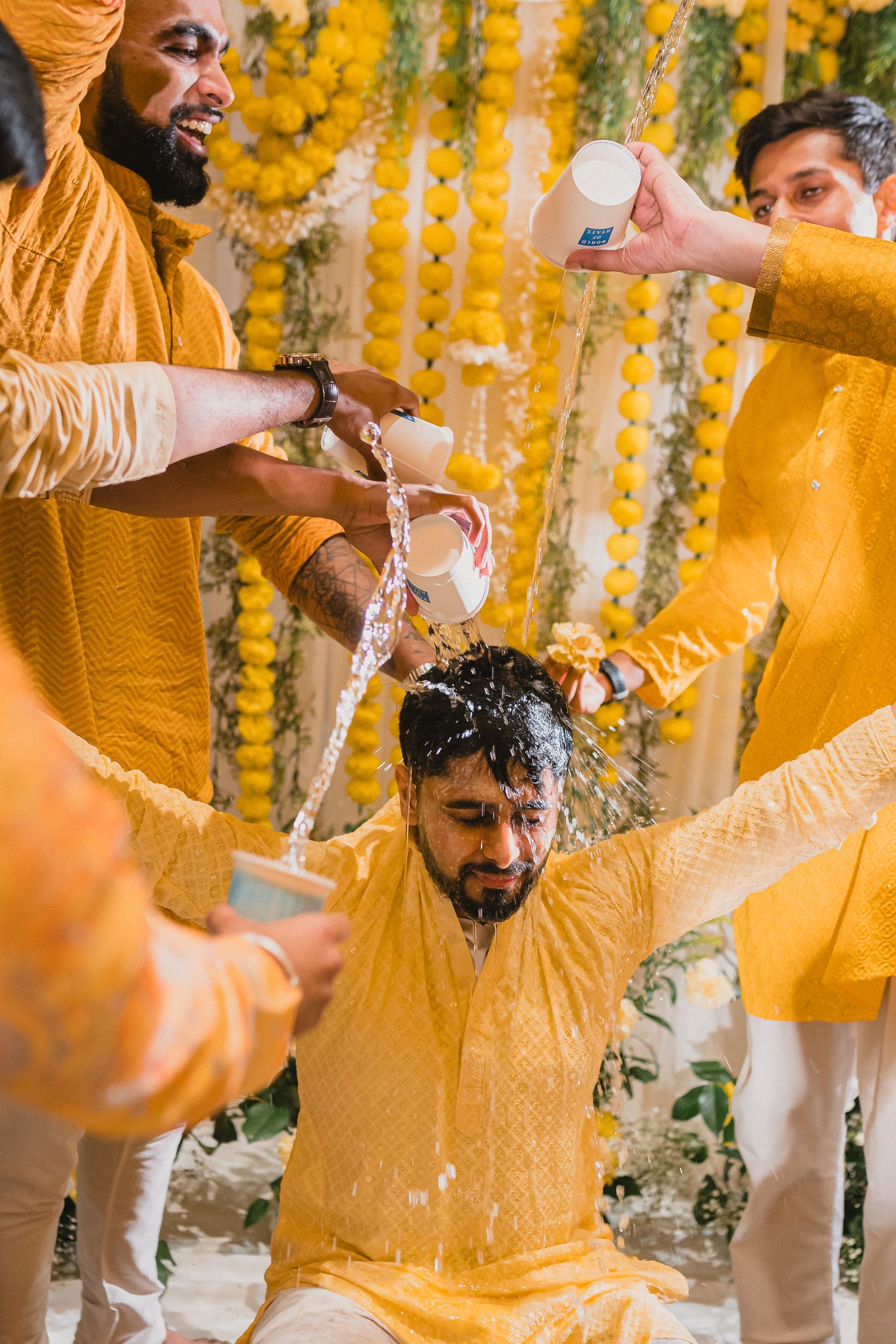 Traditional pre-wedding haldi ceremony celebration with yellow decor and participants pouring turmeric paste in festive atmosphere.