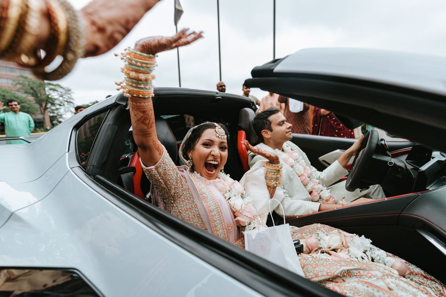 Joyous passengers celebrate with raised hands in an open-top convertible car at a festive occasion.