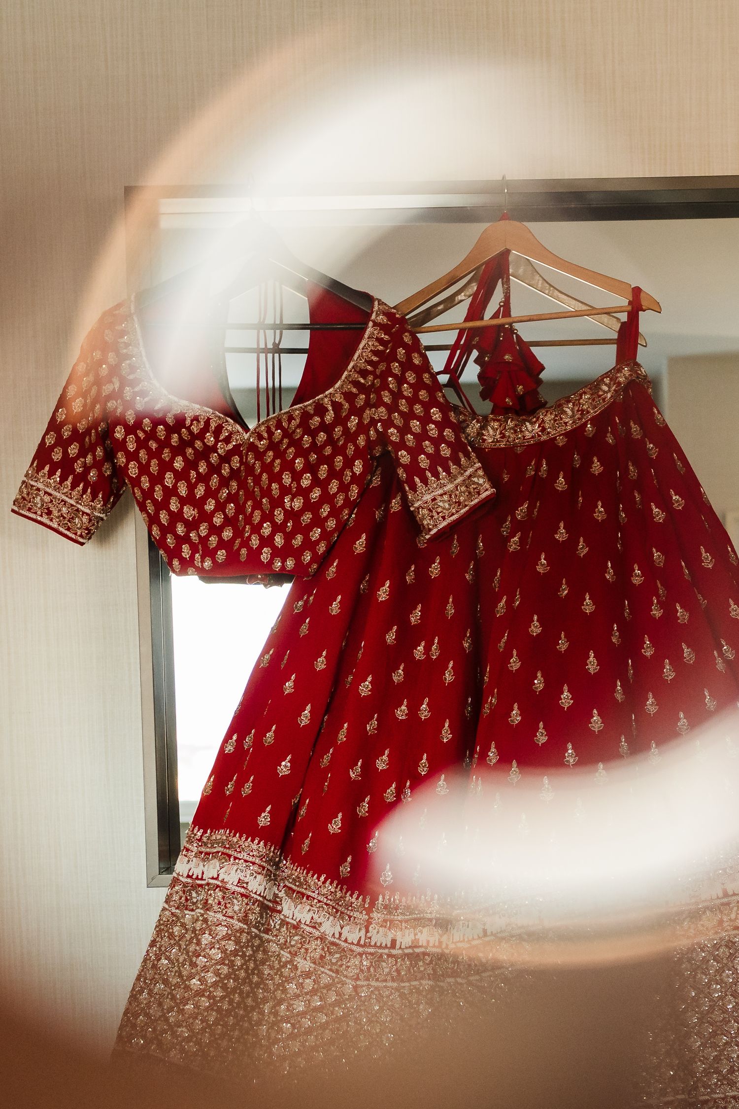 Red and gold embroidered traditional Indian lehenga and blouse hanging on display.