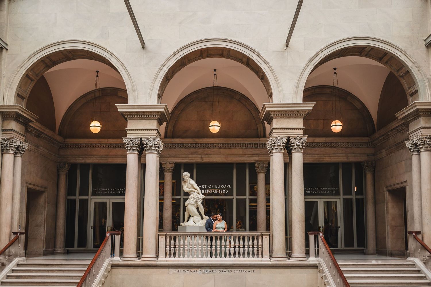 Classical arched colonnade with pendant lights and a statue in an elegant courtyard setting.
