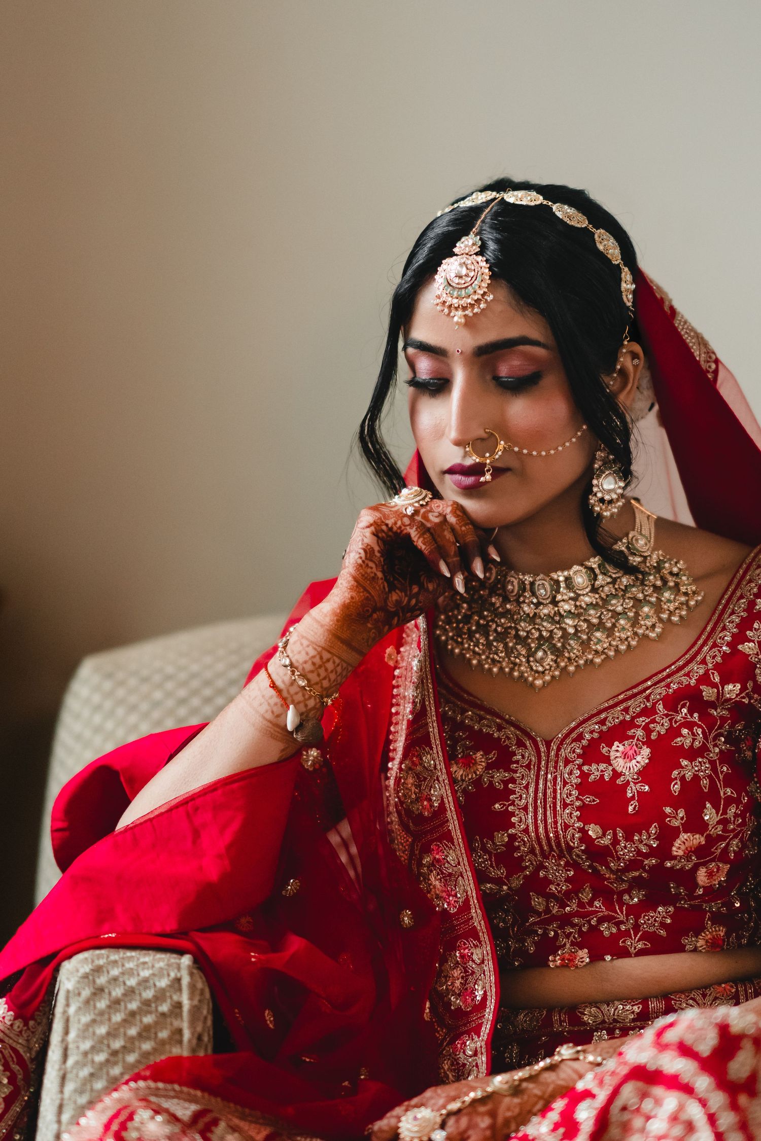 Traditional Indian bridal attire with gold necklace, red lehenga, and mehndi-adorned hands.