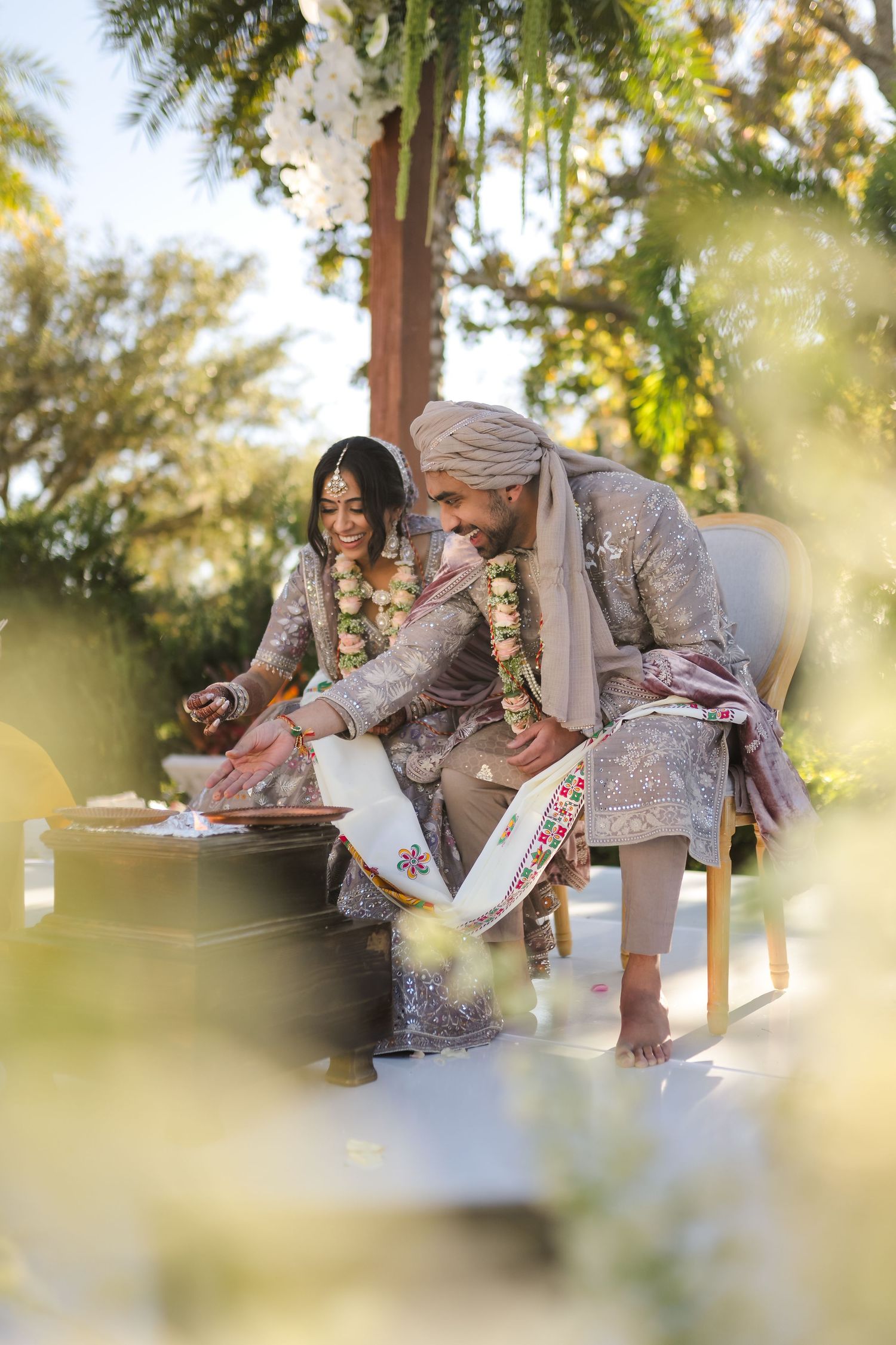 Two individuals in traditional attire share a joyous moment while seated outdoors during a cultural celebration.