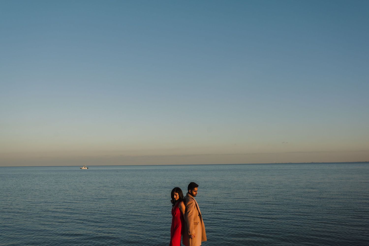 A silhouetted couple stands against a serene ocean horizon during sunset.