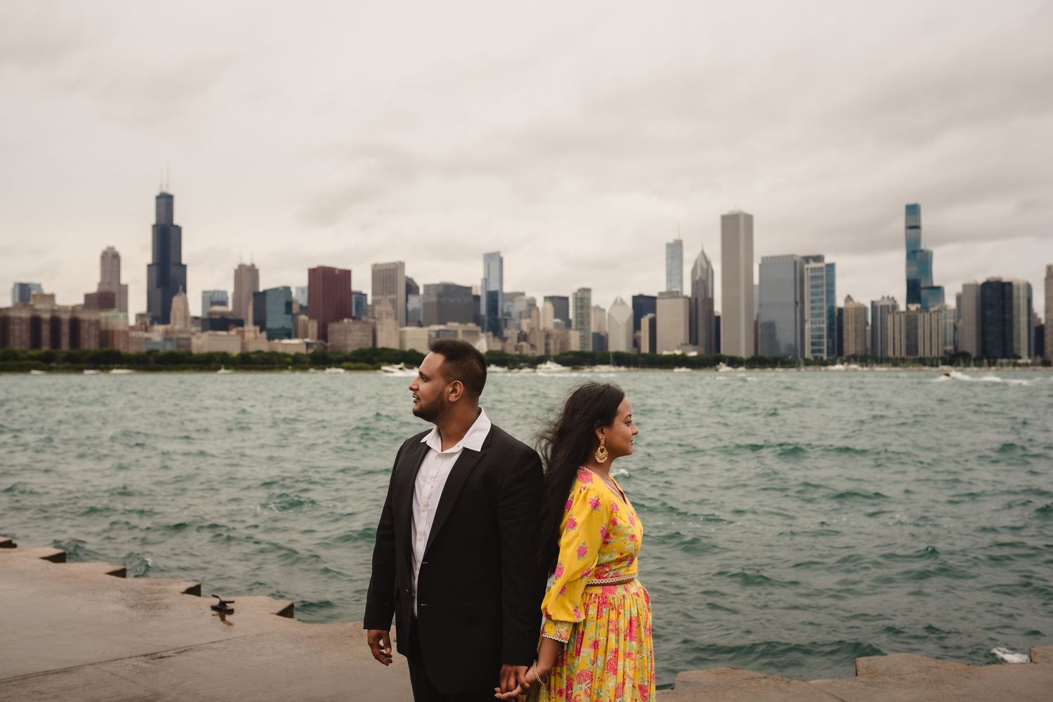 A couple stands at the lakefront with the iconic Chicago skyline backdrop on a cloudy day.