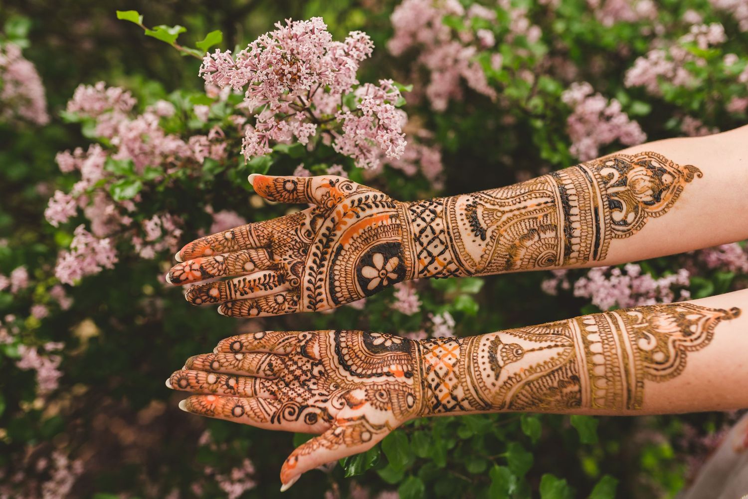 Intricate henna design decorates hands against pink floral backdrop.
