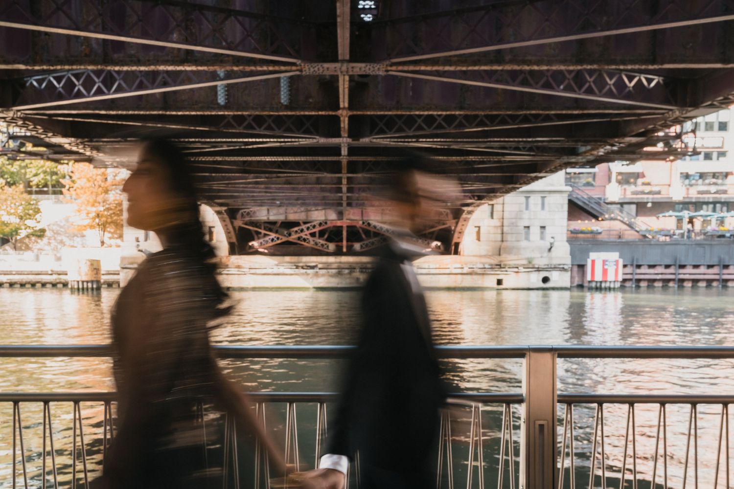 Silhouettes create a moody scene under bridge architecture near waterfront buildings.