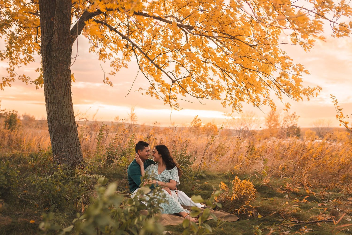 Romantic autumn scene with couple sitting under tree with orange foliage at golden hour.