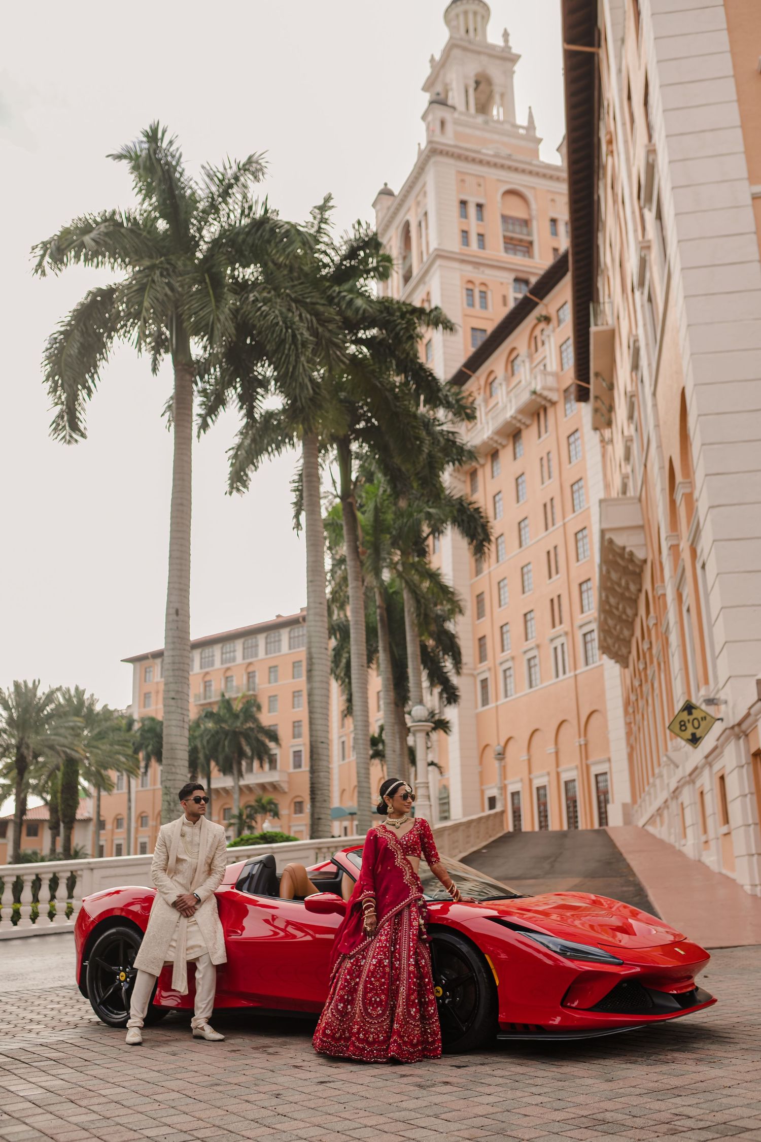 Luxury red Ferrari parked in front of grand hotel with towering palm trees and classic architecture.