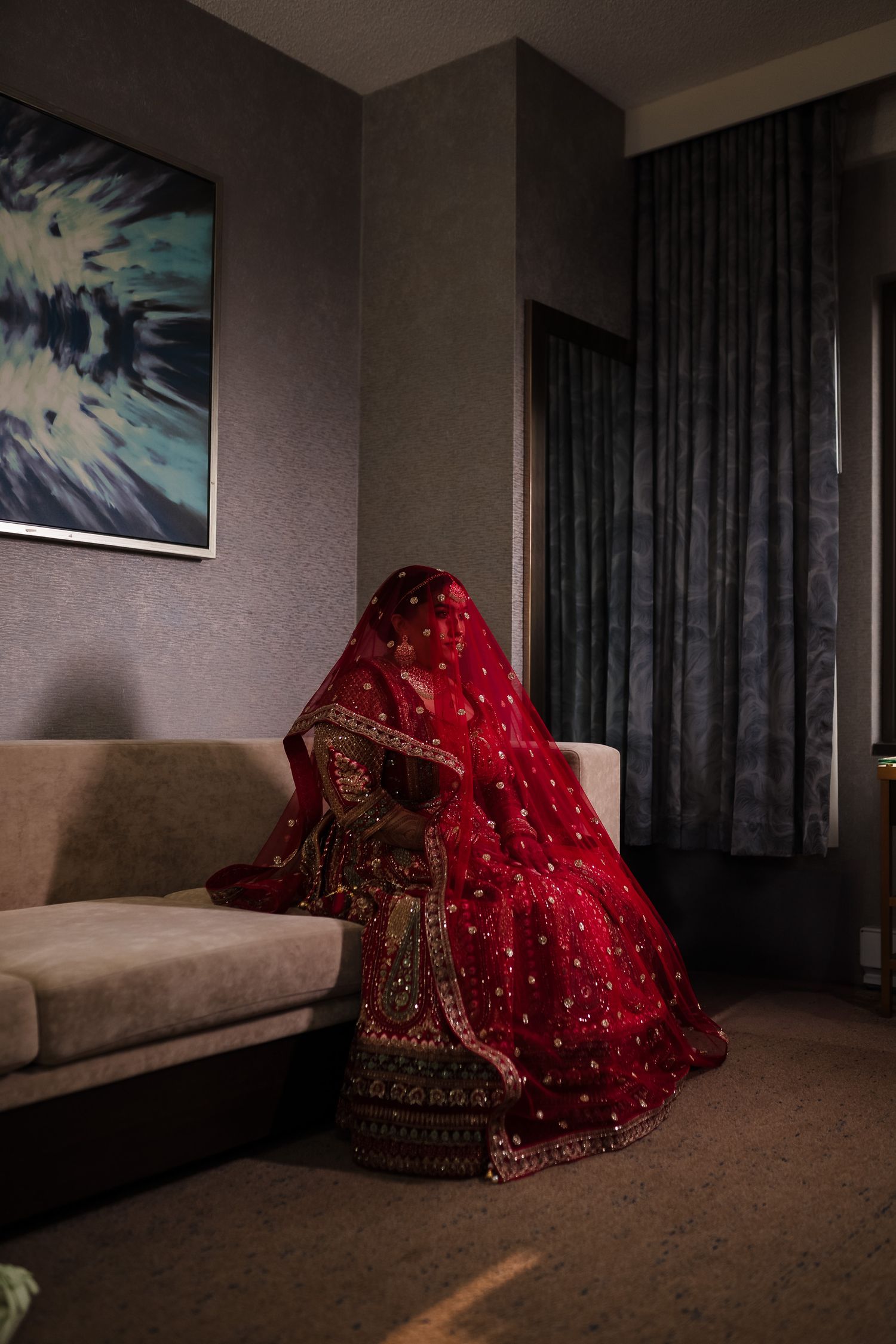 A traditional red Indian bridal lehenga with intricate embroidery and sparkles sits in a modern living room setting.