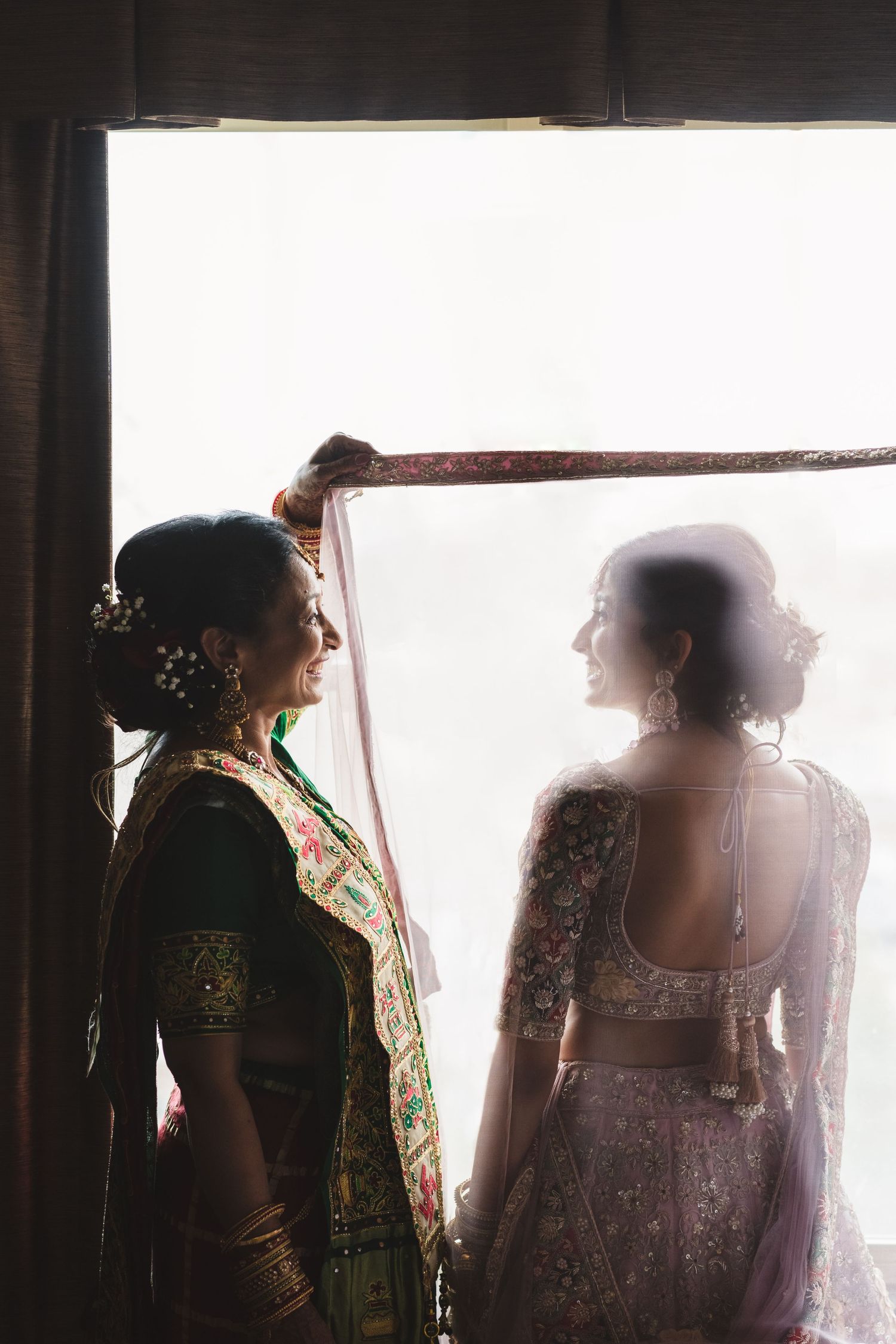 Artistic silhouette of two figures in traditional Indian attire sharing intimate moment by window.