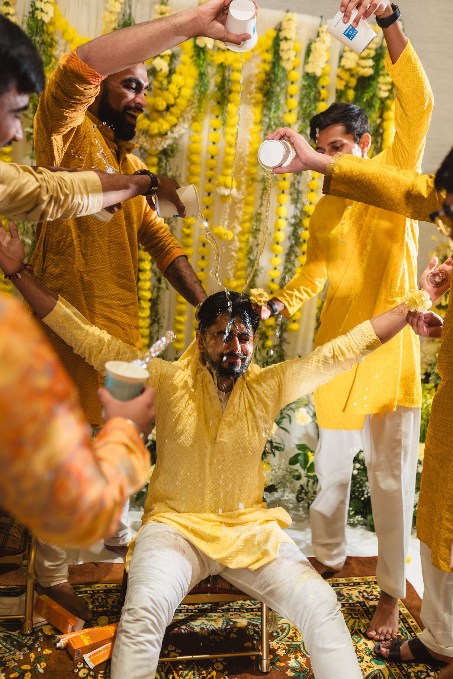 Joyful celebration at an Indian haldi ceremony with yellow decorations and turmeric being applied during pre-wedding rituals.
