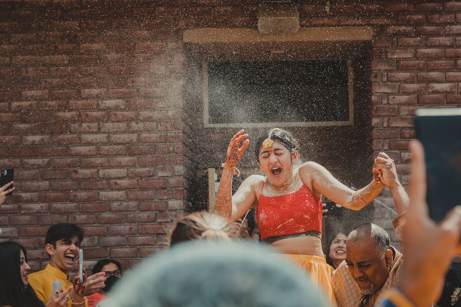 People celebrating at an outdoor gathering with colored powder in front of a brick wall during a festival celebration.