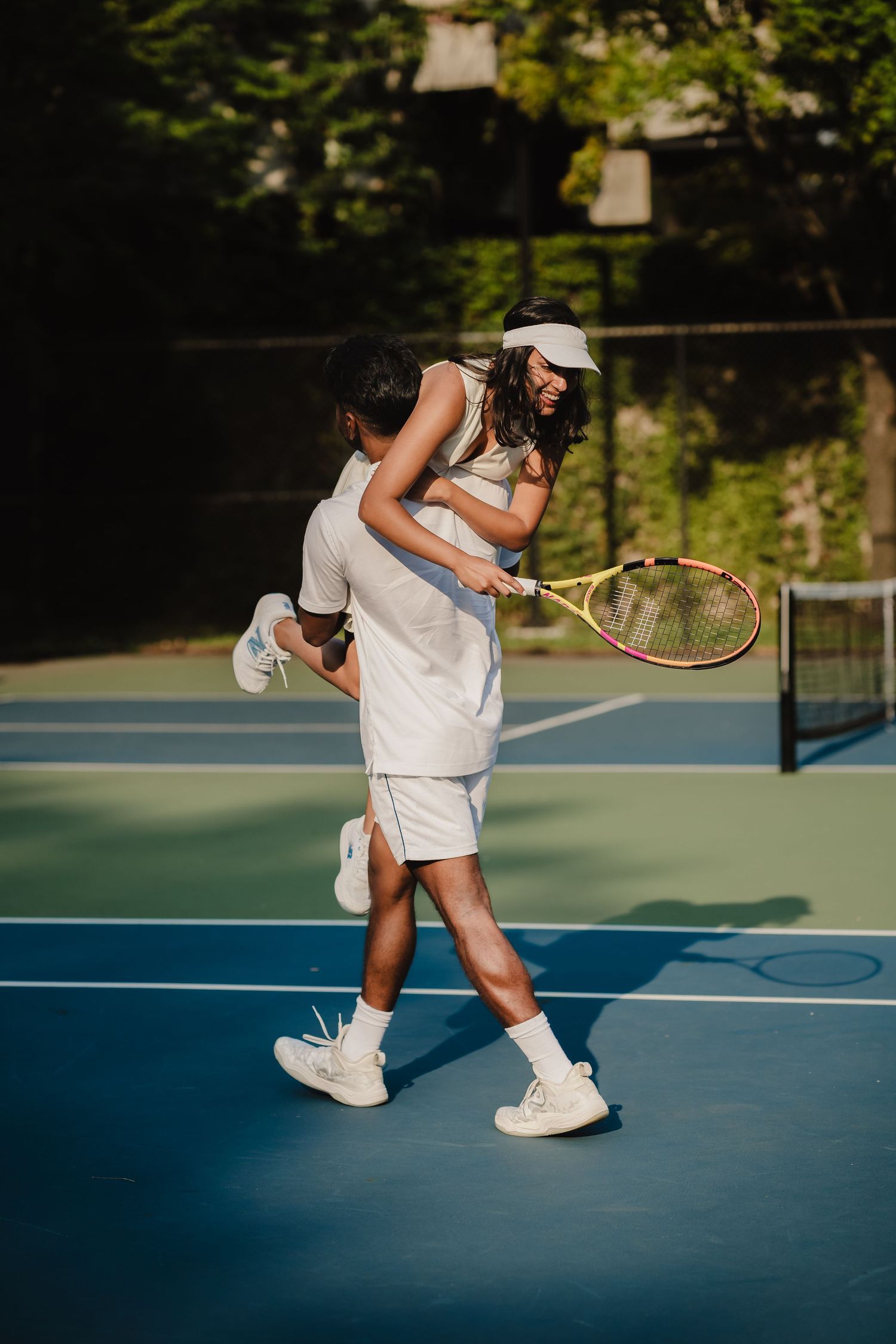 Two people share a playful moment on a blue tennis court during a sunny afternoon game.