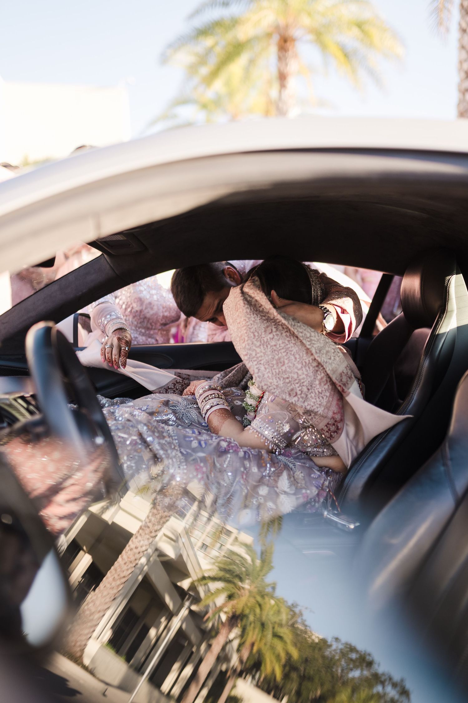 A detailed view through a car window showing traditional South Asian bridal attire with palm trees in background.