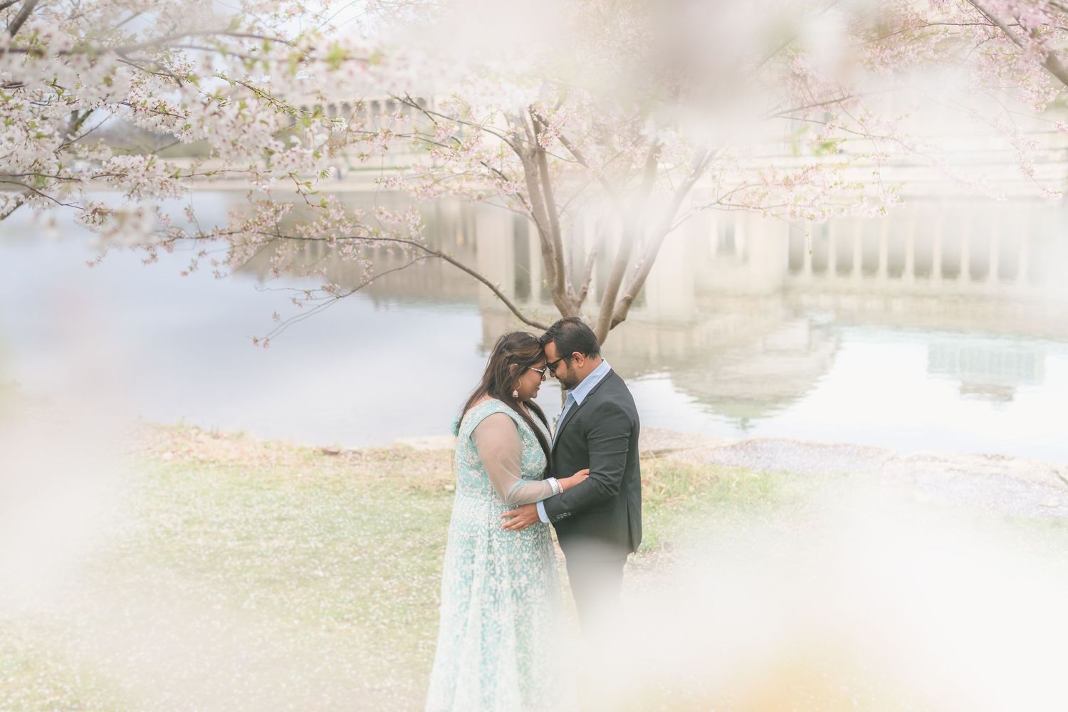 A romantic couple embraces under blooming cherry blossoms on a misty spring day with soft dreamy lighting.