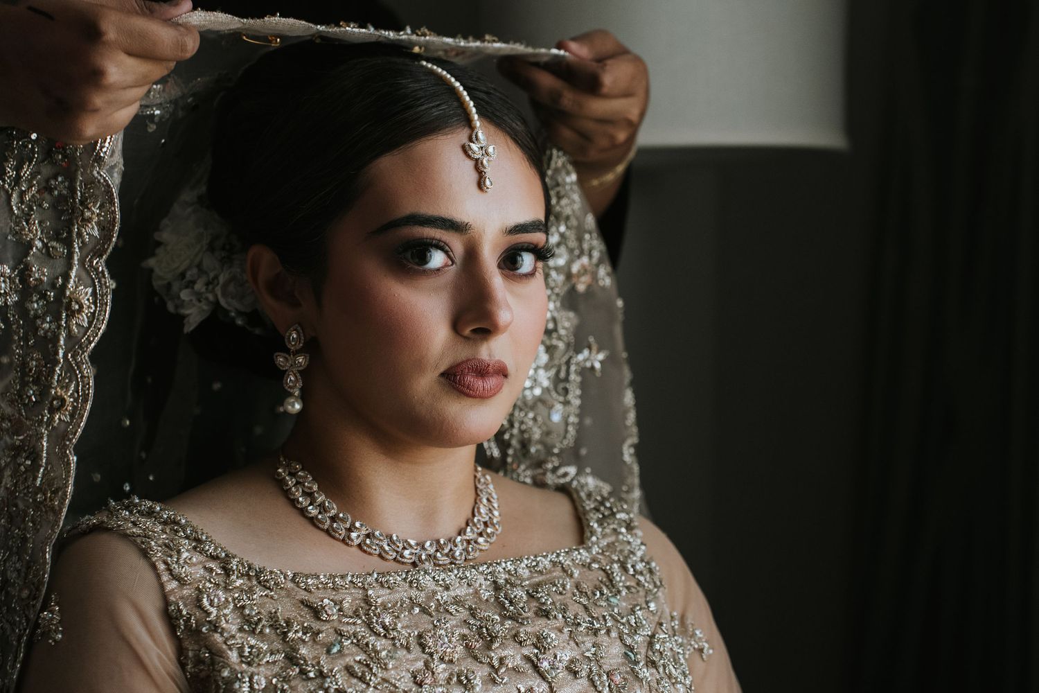 Elegant bridal portrait showcasing detailed beadwork and jewelry against dark background.
