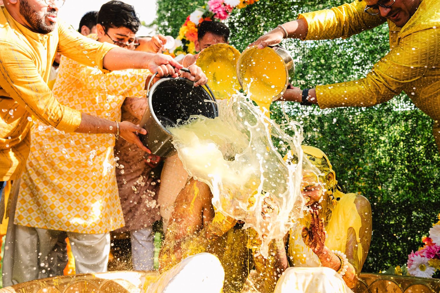 Traditional Indian wedding celebration with people wearing yellow kurtas splashing water and milk during festive rituals outdoors.