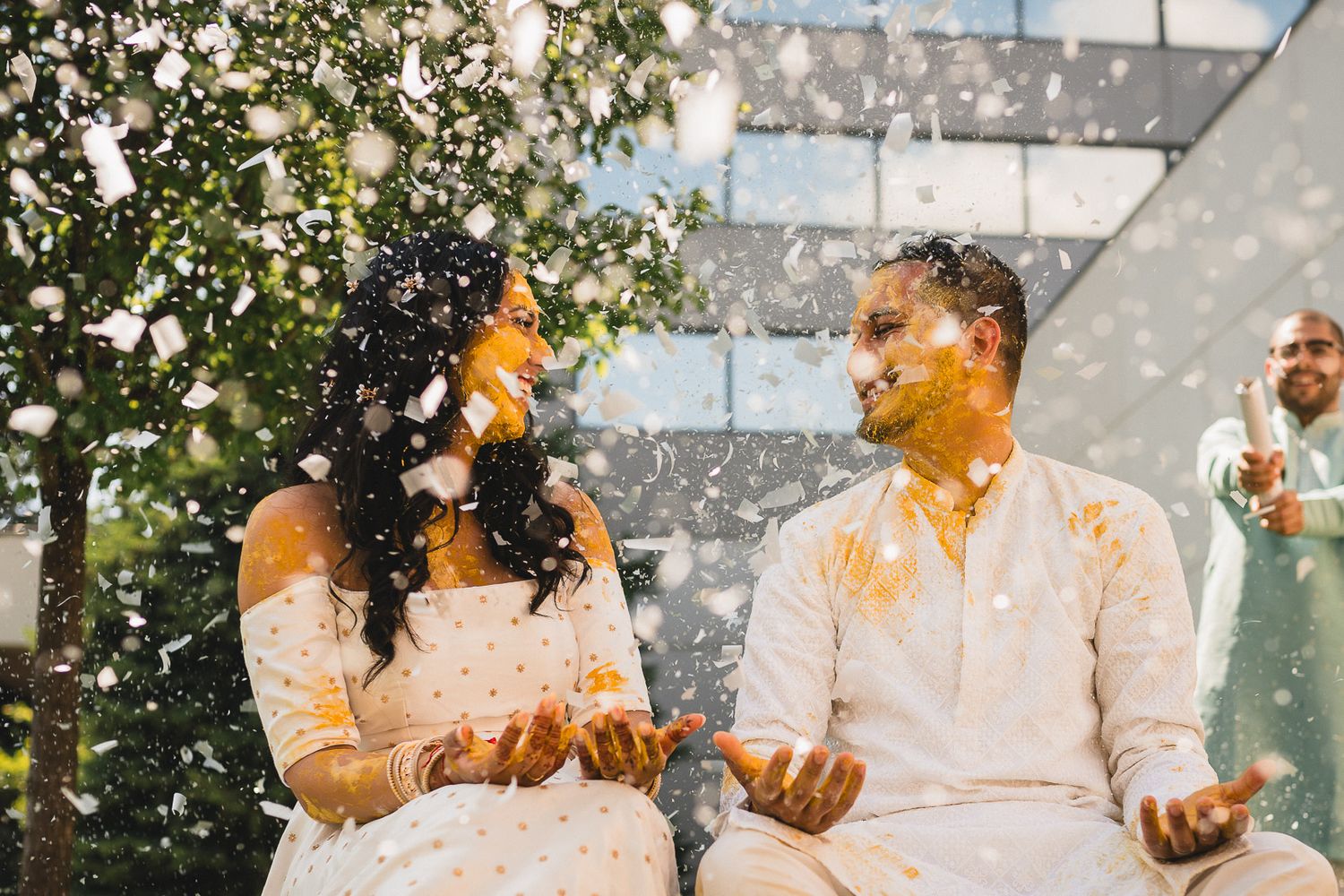 Couple laughs joyfully as they're showered with yellow turmeric powder during a traditional Haldi ceremony celebration.