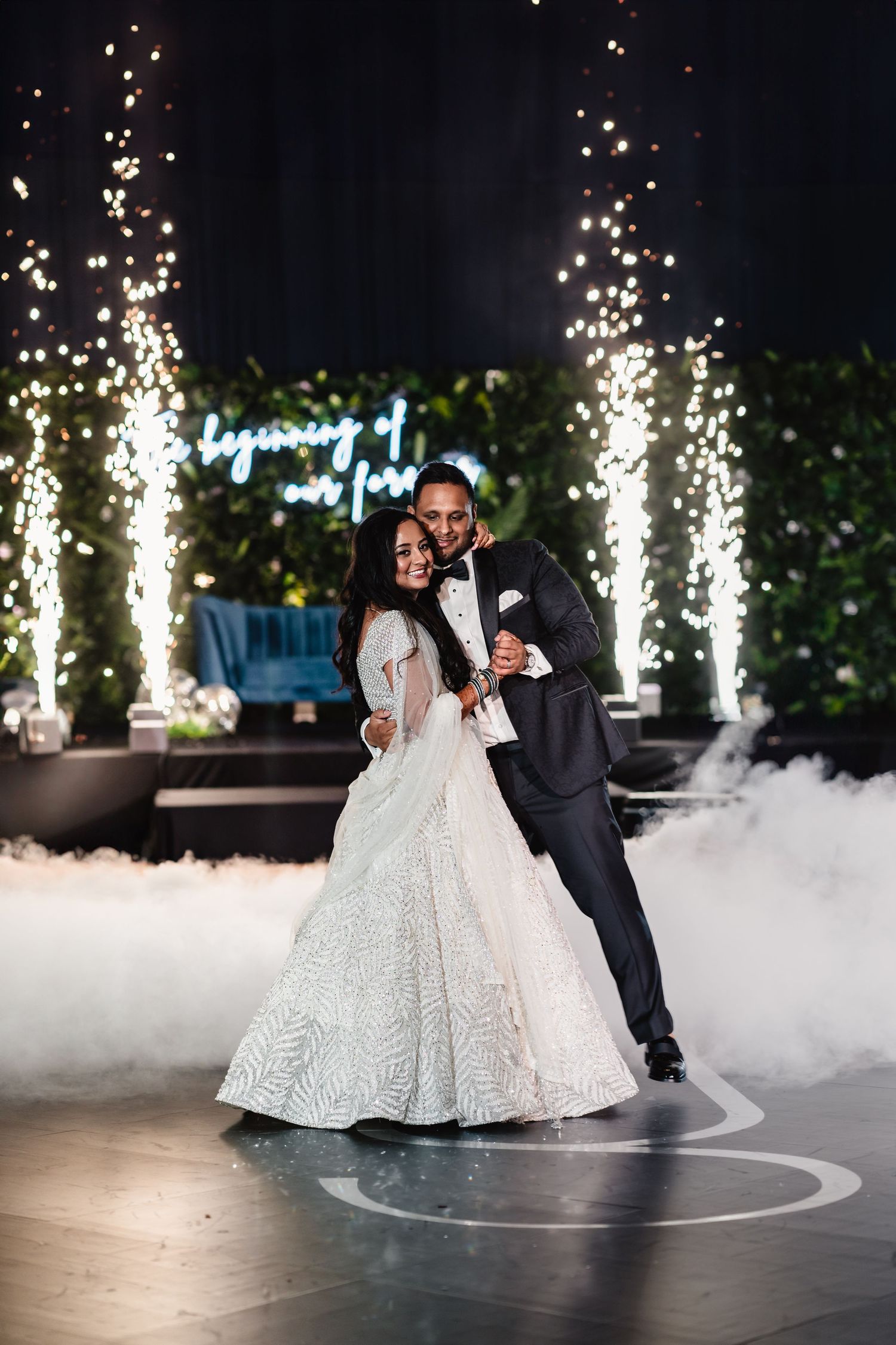 Wedding couple dancing amid sparklers and fog effects on an illuminated dance floor.