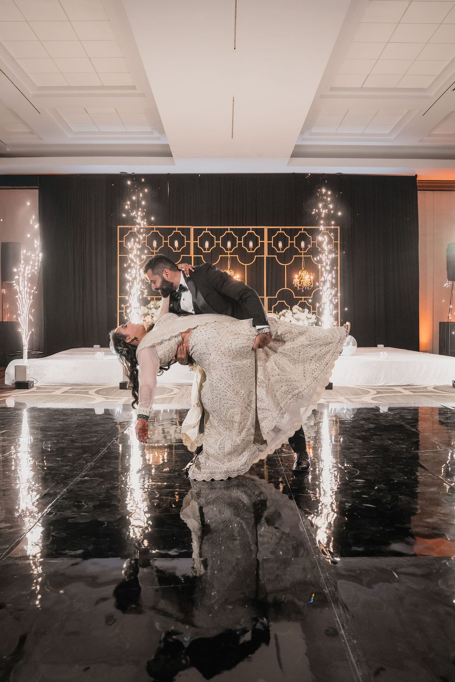 Romantic wedding dance pose with sparklers and dramatic lighting on reflective floor.