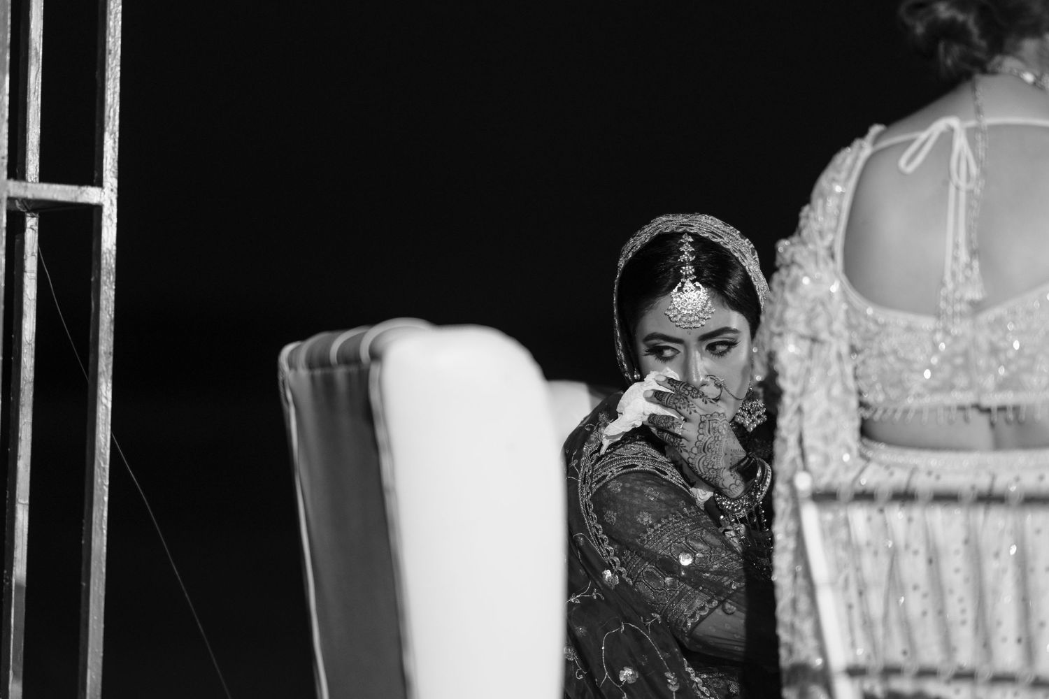 A black and white artistic portrait showing a person wearing ornate South Asian bridal attire.