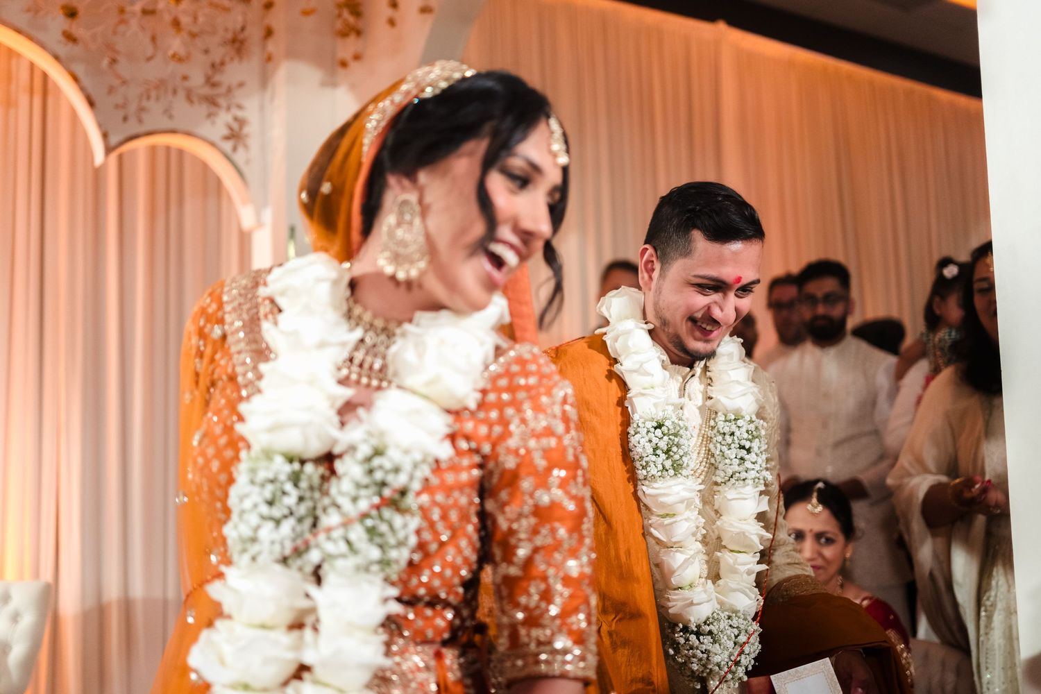 A couple in traditional South Asian wedding attire share a joyful moment during their ceremony, adorned with flower garlands.
