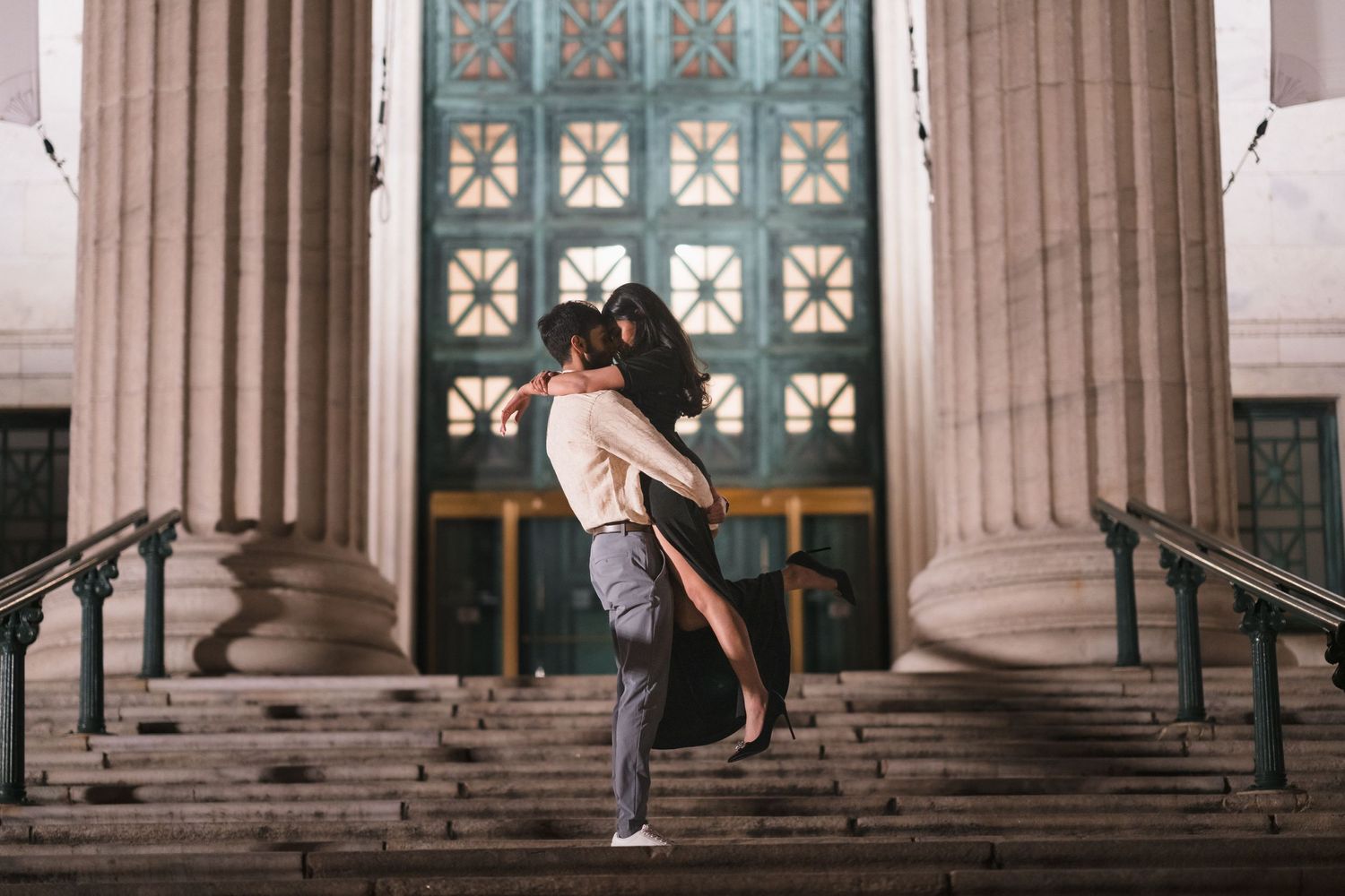 A romantic embrace on the steps of a historic building with ornate columns and doors.