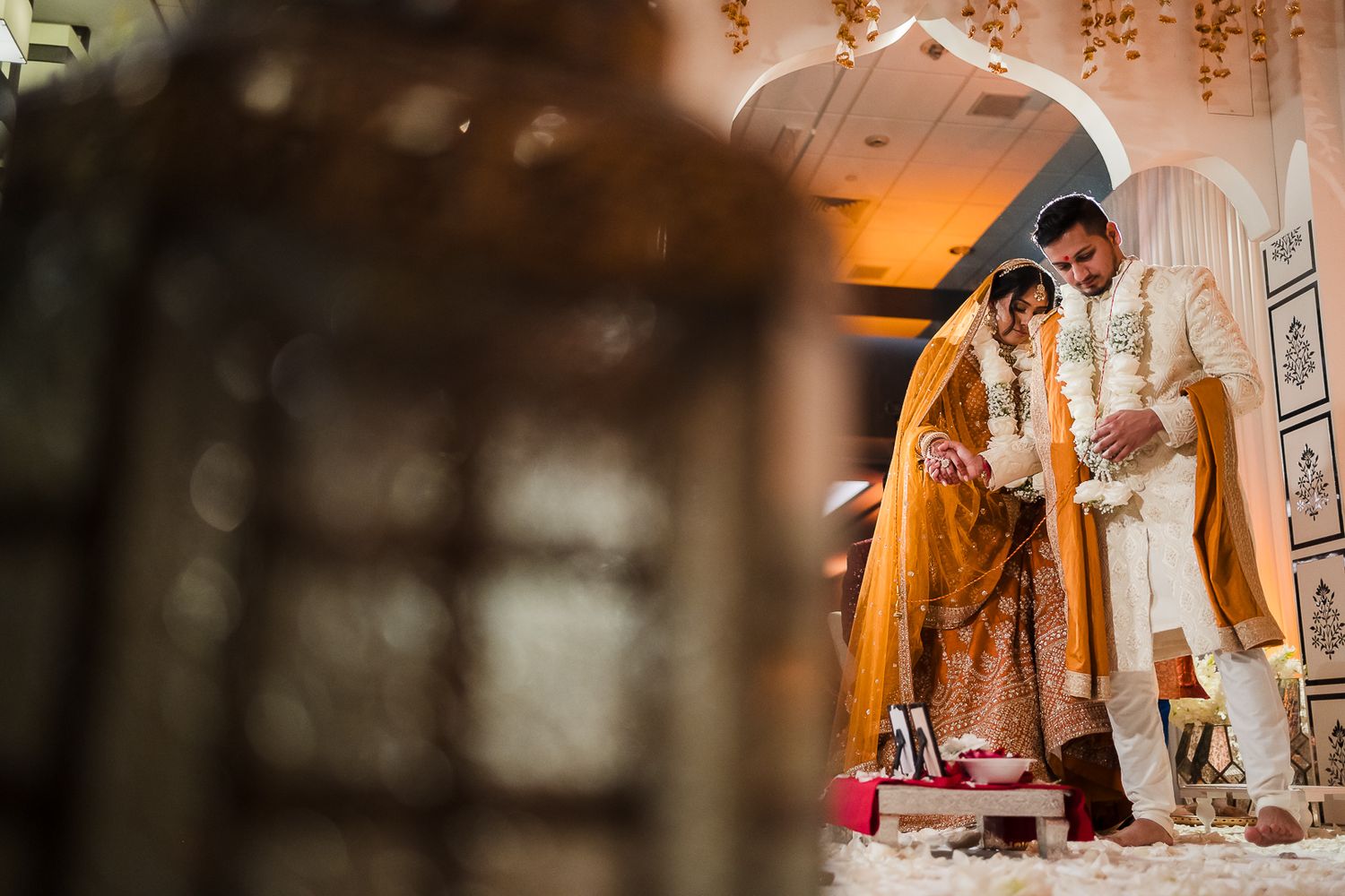 Traditional South Asian wedding ceremony with ornate decor and warm sunset lighting through an arched doorway.