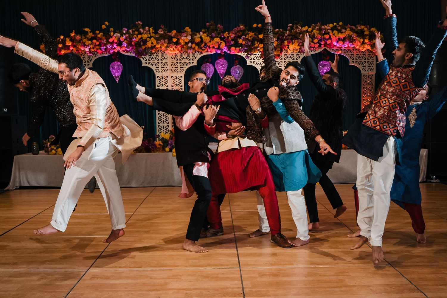 Dancers strike fun poses during an energetic group dance performance at a wedding reception with floral decor.