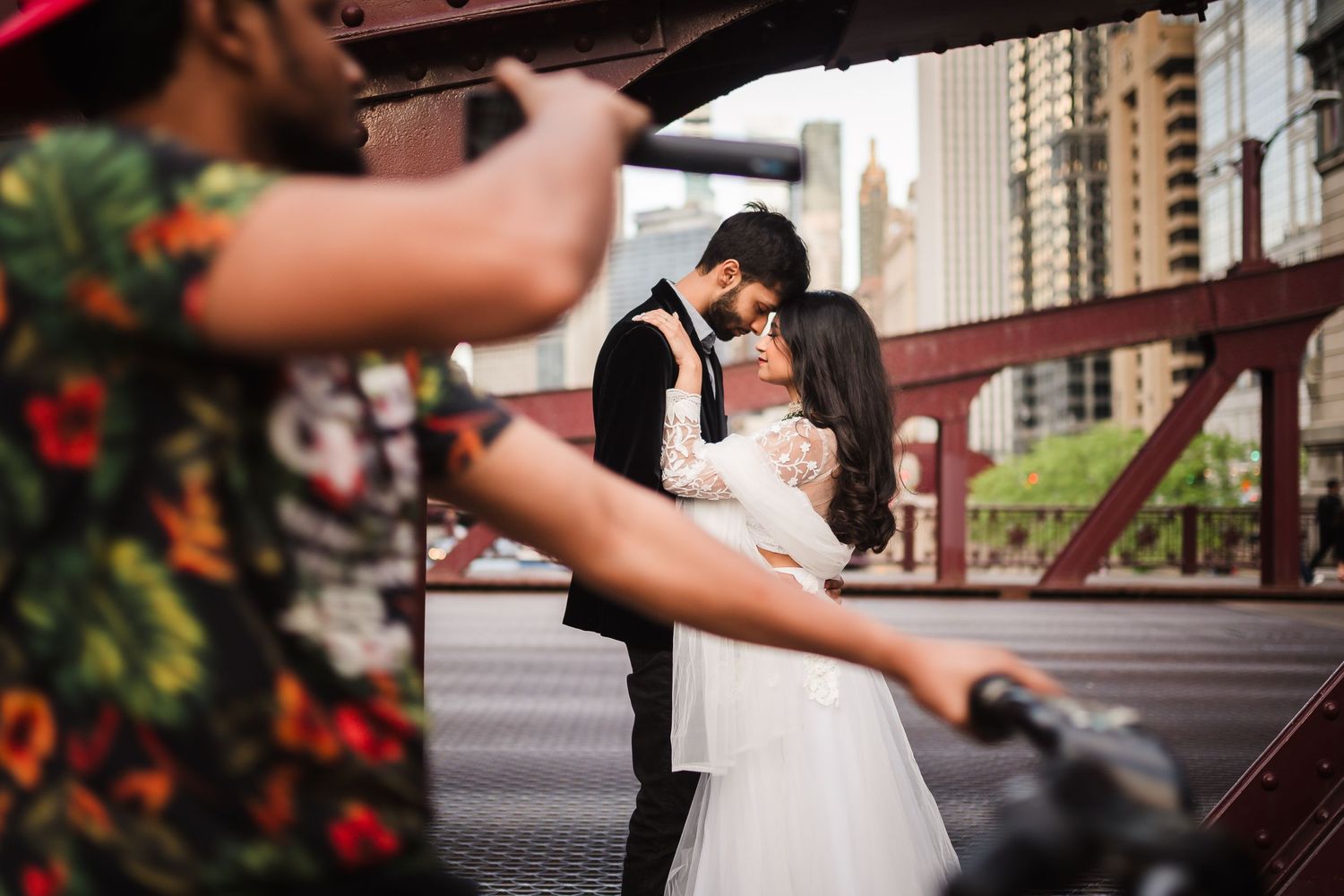 A couple sharing a romantic moment on an urban bridge while being photographed.
