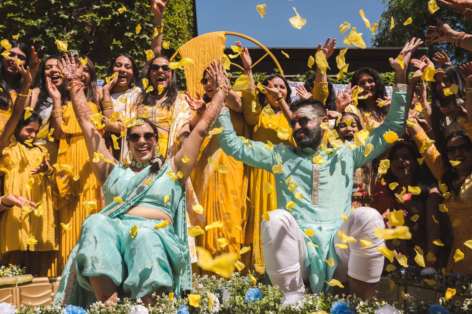 Wedding celebration with confetti flying as people in yellow and turquoise outfits celebrate joyfully outdoors.