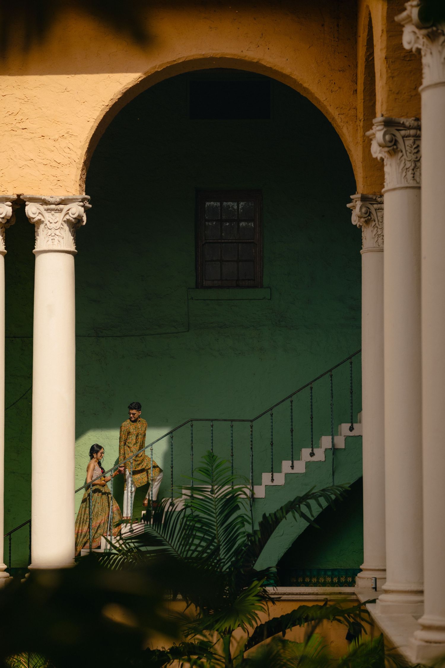 Artistic wedding portrait under arched colonnade with white pillars against emerald green wall.