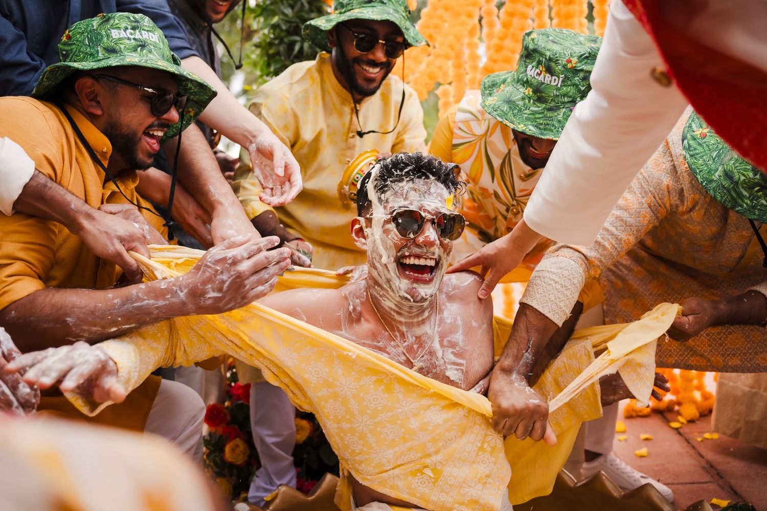 People playfully smear colored powder during Holi festival celebrations while seated on yellow fabric outdoors.