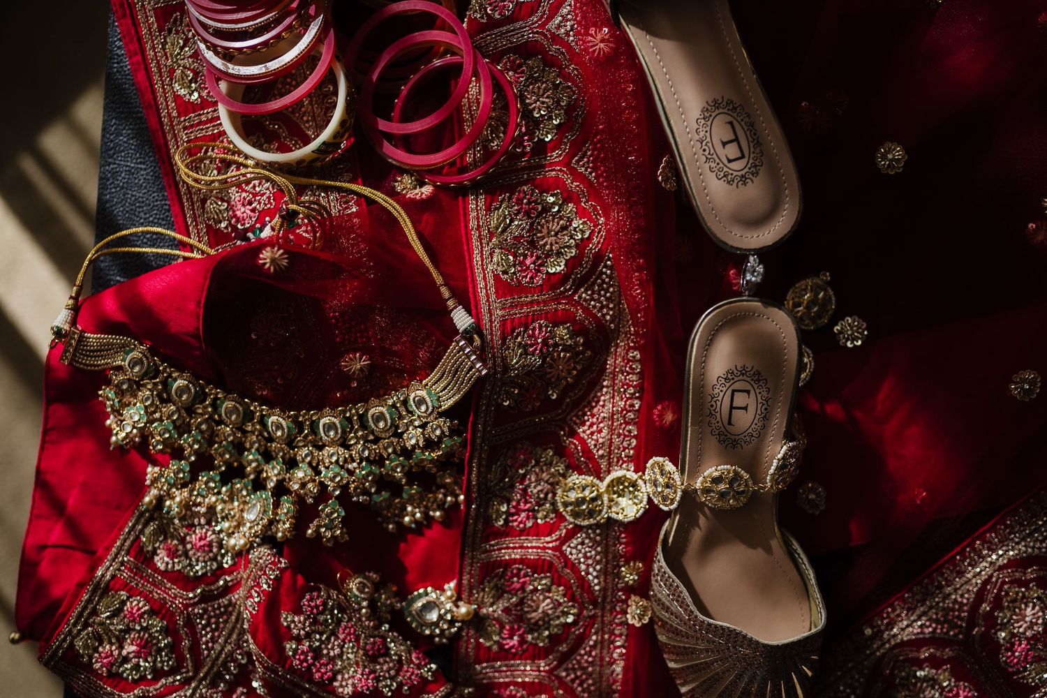 Traditional Indian bridal accessories including silver heels, ornate jewelry, and red fabric with detailed embroidery.