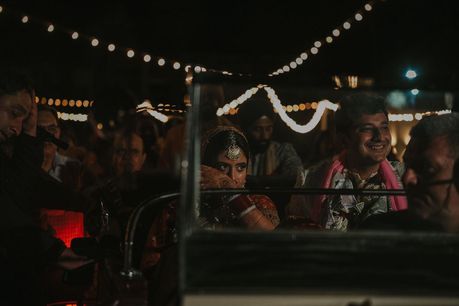 A dark nighttime scene with string lights overhead and a crowd gathered at an outdoor event.