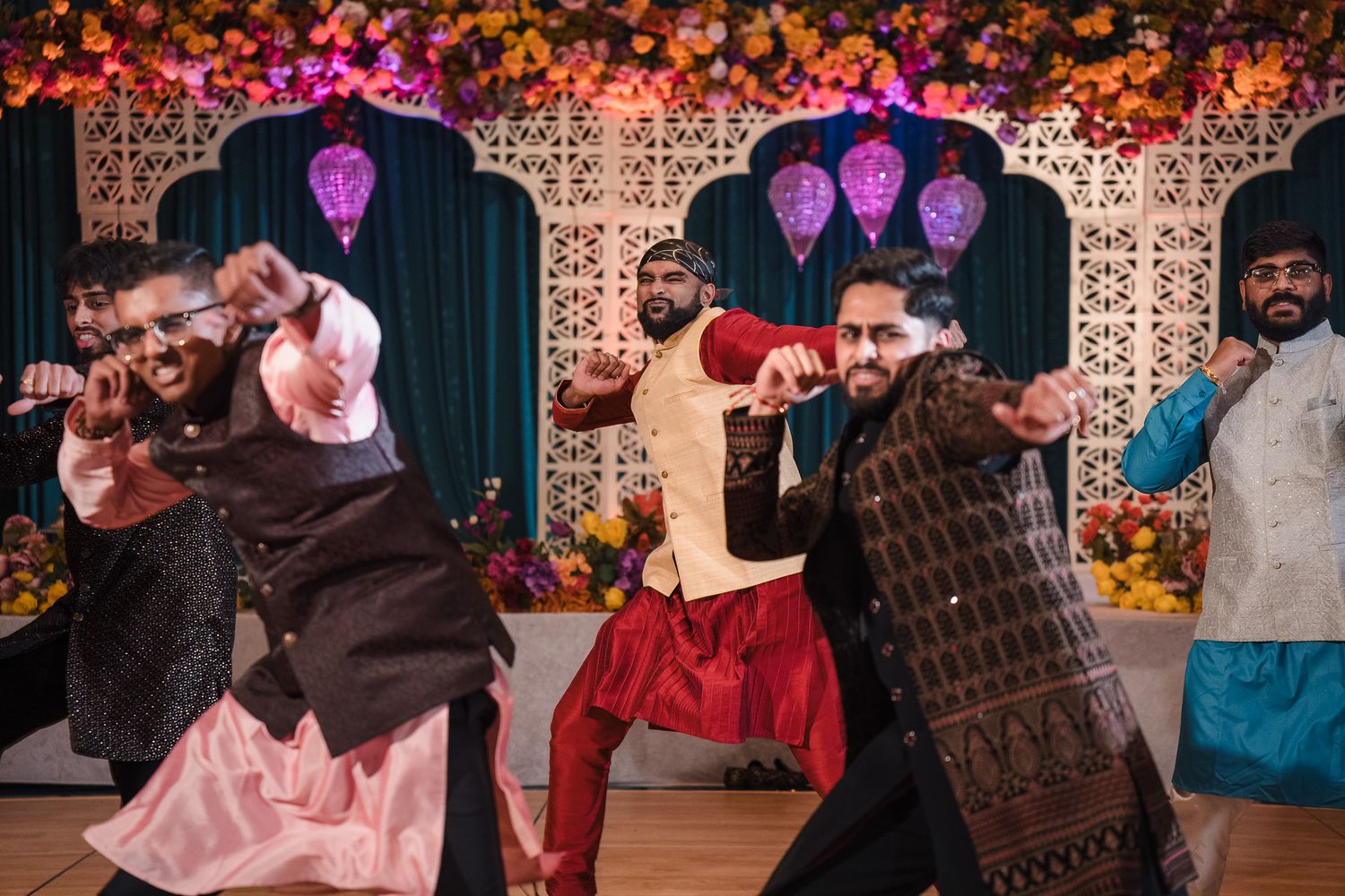 Dancers perform energetic moves at a colorful wedding celebration with neon skull decorations and floral backdrop.