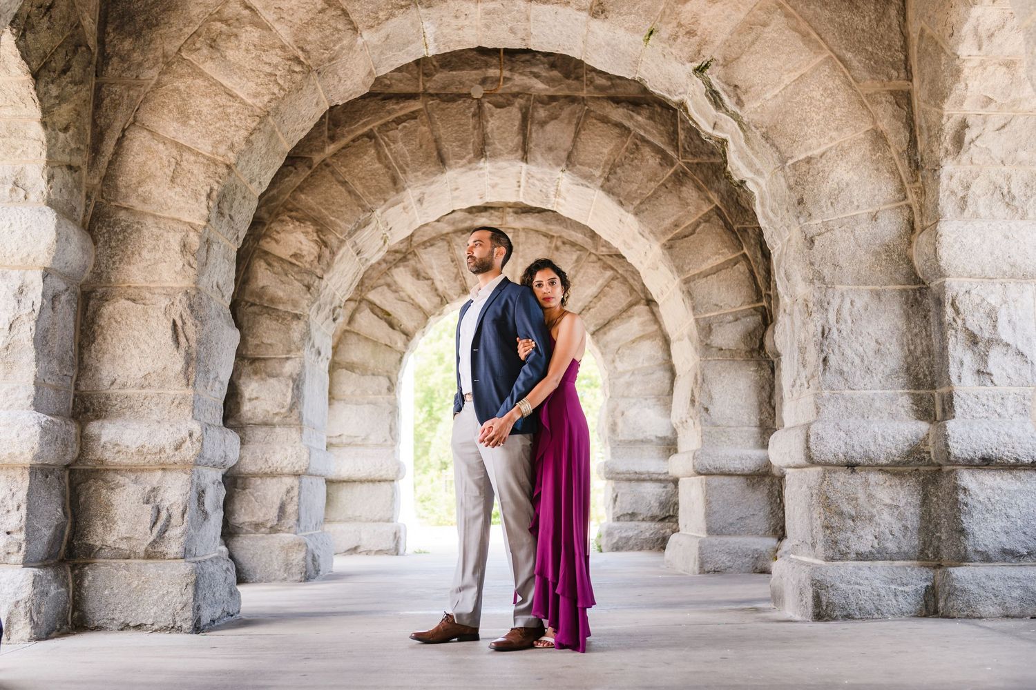 A romantic couple poses under a grand stone archway.