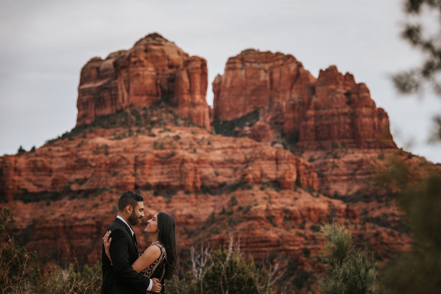 A couple embraces in front of the majestic red rock formation of Cathedral Rock in Sedona, Arizona.