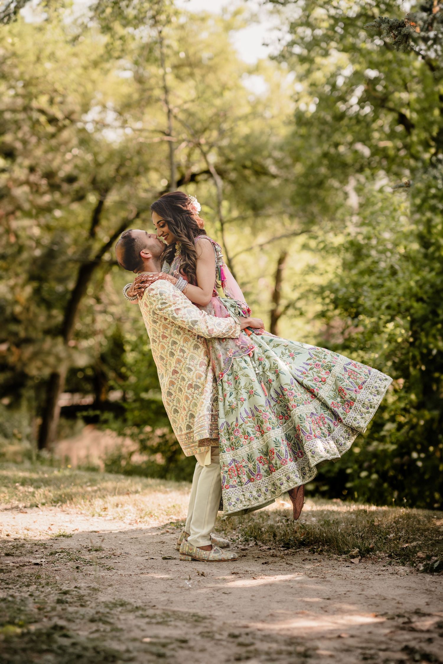 Romantic couple embraces in a dreamy forest setting wearing traditional South Asian wedding attire.