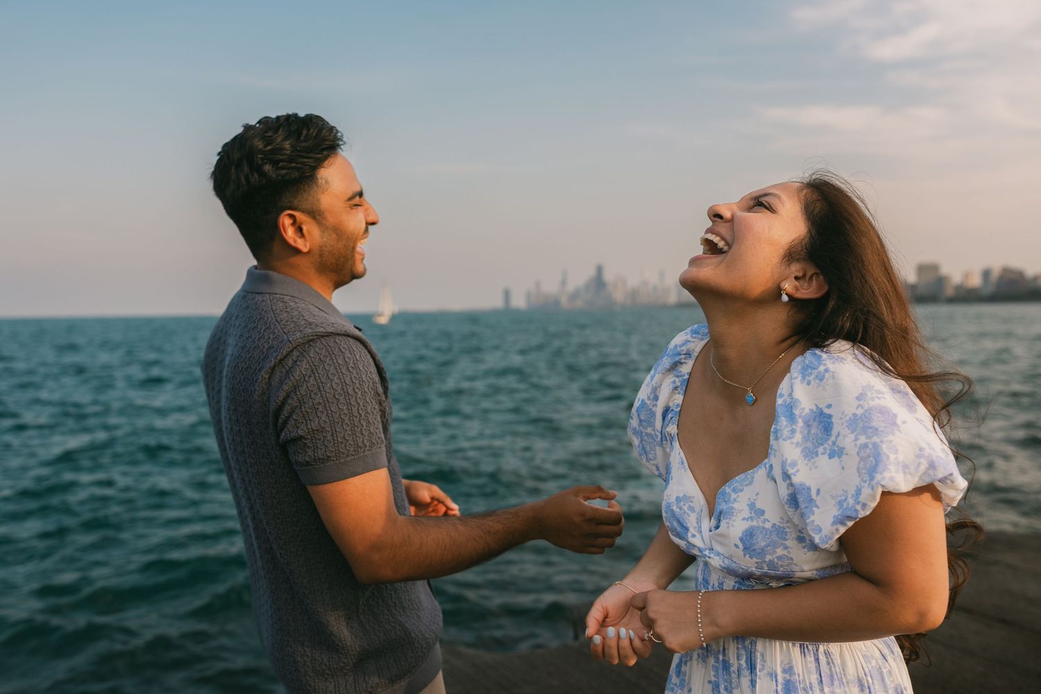 Romantic couple laughing and embracing by the ocean at sunset while enjoying a waterfront moment together.