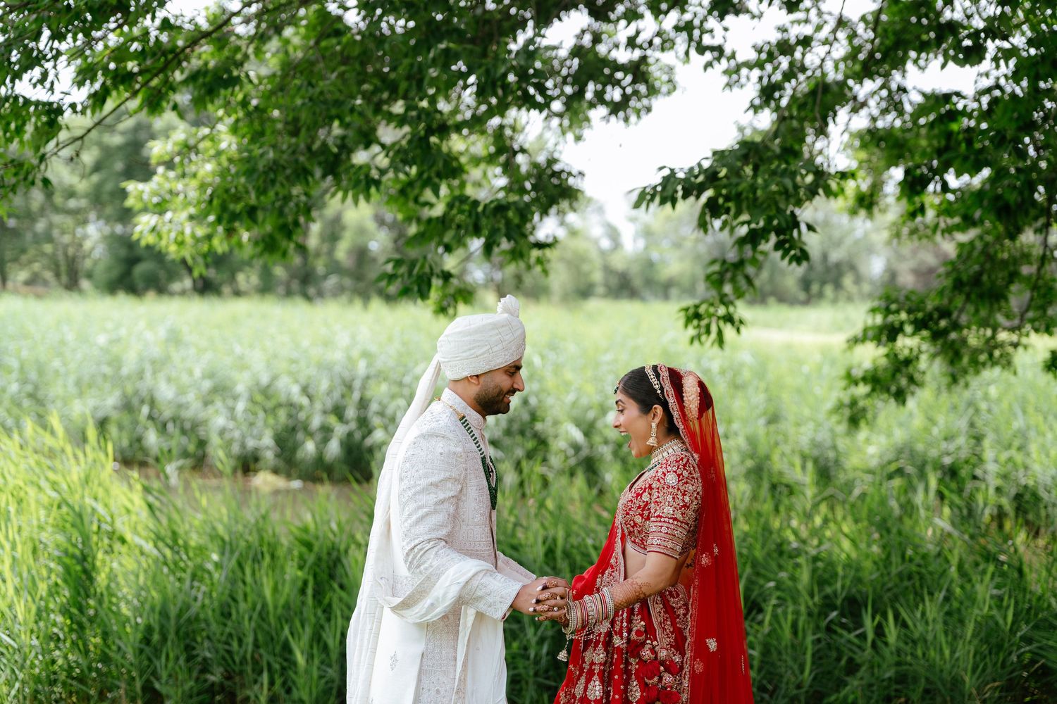 Traditional Punjabi wedding couple shares an intimate moment together in a lush green outdoor setting.